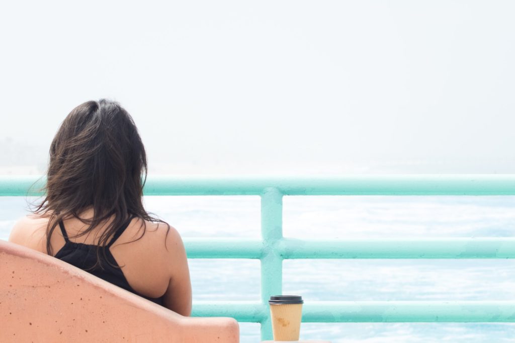 woman sitting on chair beside cup in front of body of water